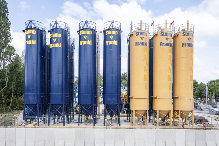 Auf der Baustelleneinrichtungsfläche steht eine Reihe etwa 20 Meter hoher, blauer und gelber Tanks.