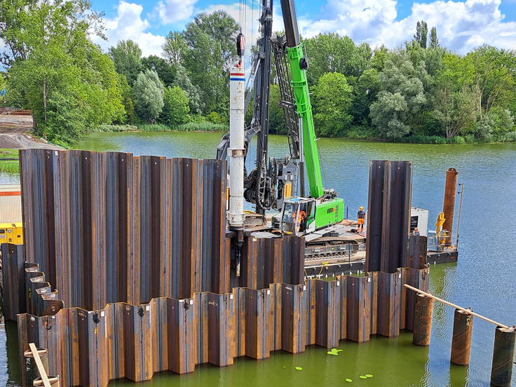 Ist der Boden zu fest, dann muss die Ramme ran: zu sehen in der Bildmitte als weißer, langer Zylinder. Mit der Hydraulikramme werden die Spundwände die letzten Meter in den Boden eingebracht.